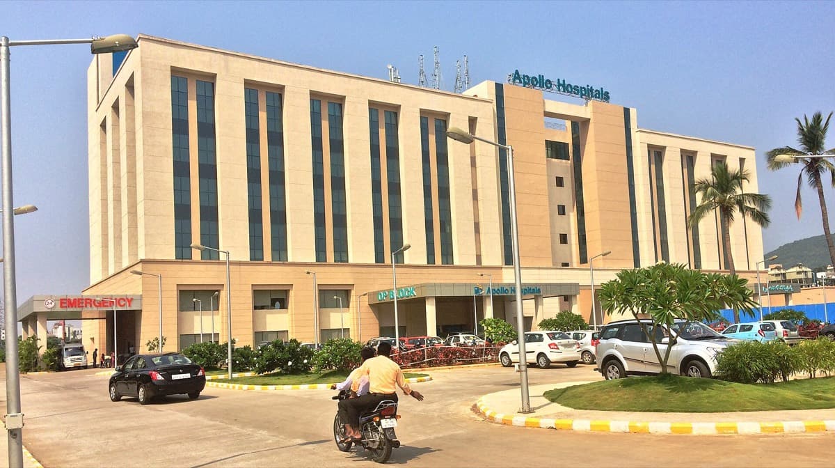 The multi-storey Apollo Hospitals building in Visakhapatnam, with a signed emergency entrance and a landscaped forecourt.