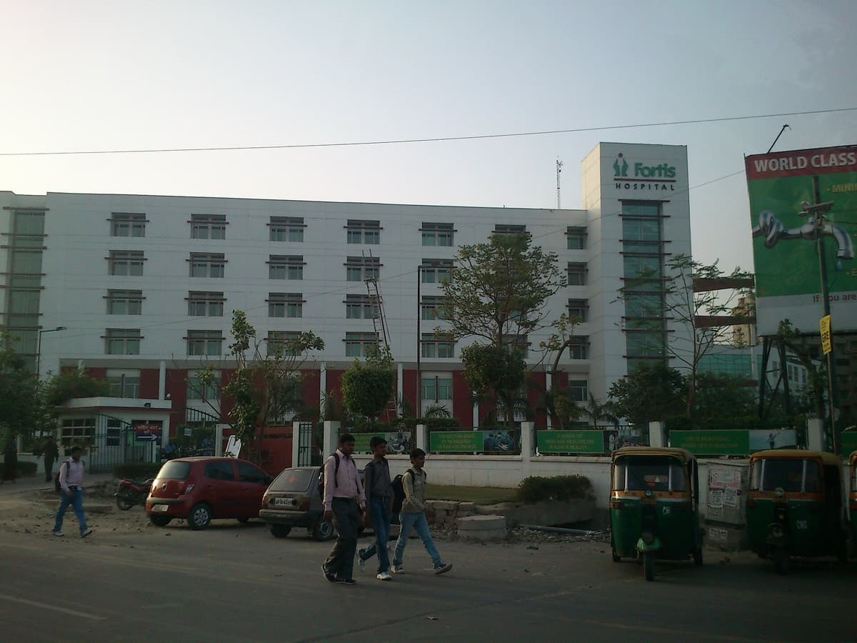 The long white frontage of Fortis Hospital in Noida seen from the road, with rooftop signage.